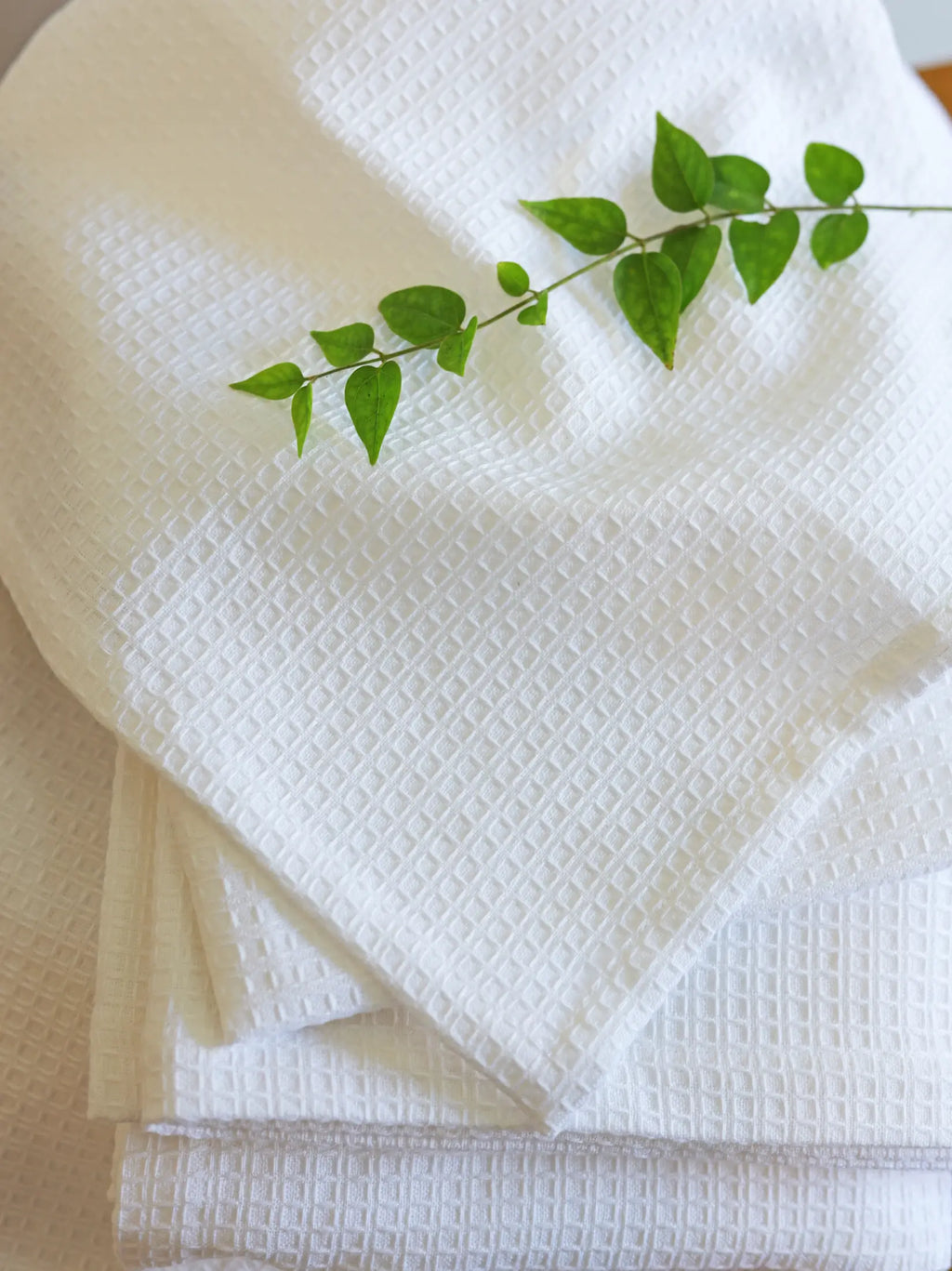 Folded white waffle towels with a green leafy sprig