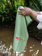 Hands holding an olive green waffle towel with bee and garden flower embroidery