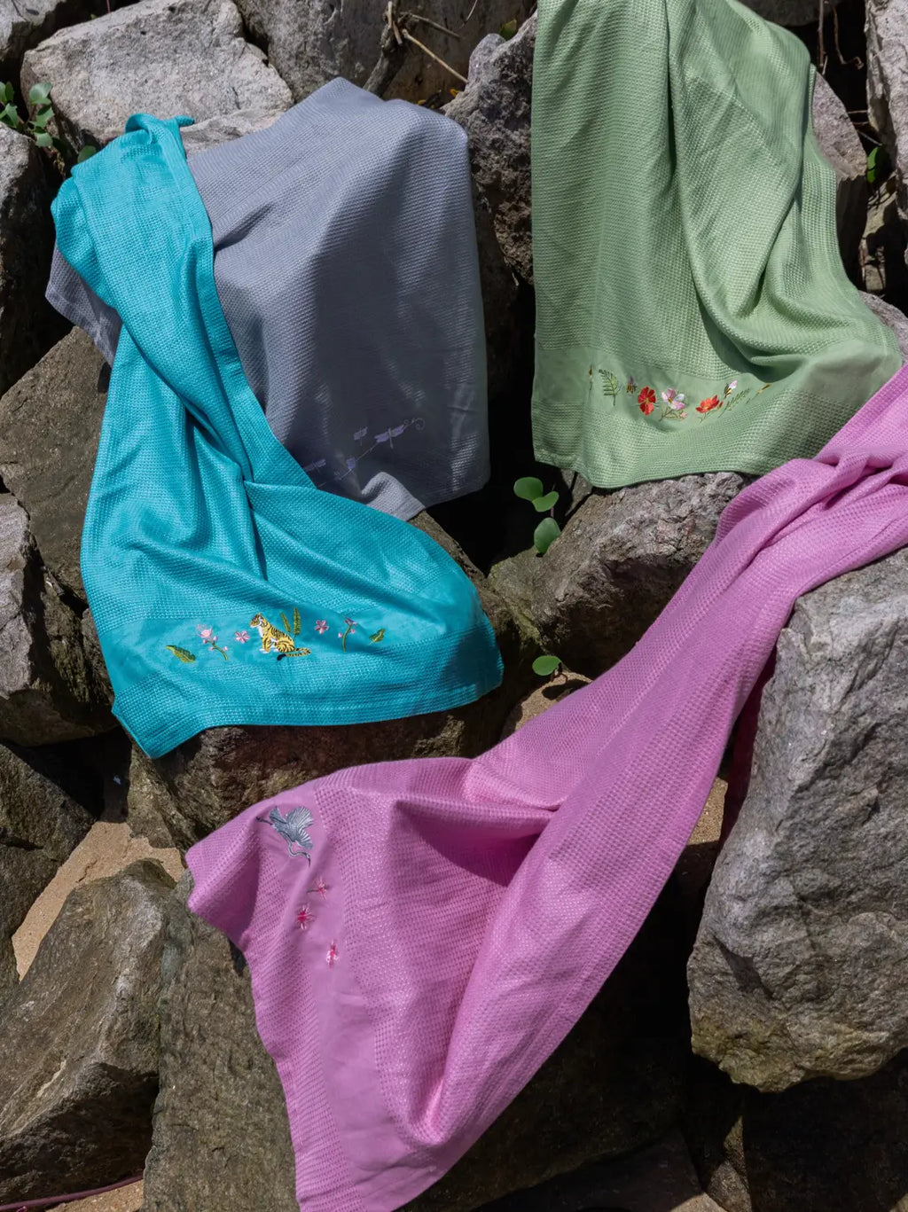 Teal, grey, olive green and mauve waffle towels with tiger, dragonfly, floral and crane embroidery on rocks
