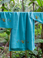Three teal blue waffle towels with tiger and flower embroidery hanging outdoors