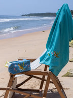 Teal blue embroidered waffle towel and matching zip pouch on a beach chair