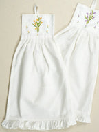 Two white hanging waffle hand towels with yellow and purple tulip embroidery and ruffled hems