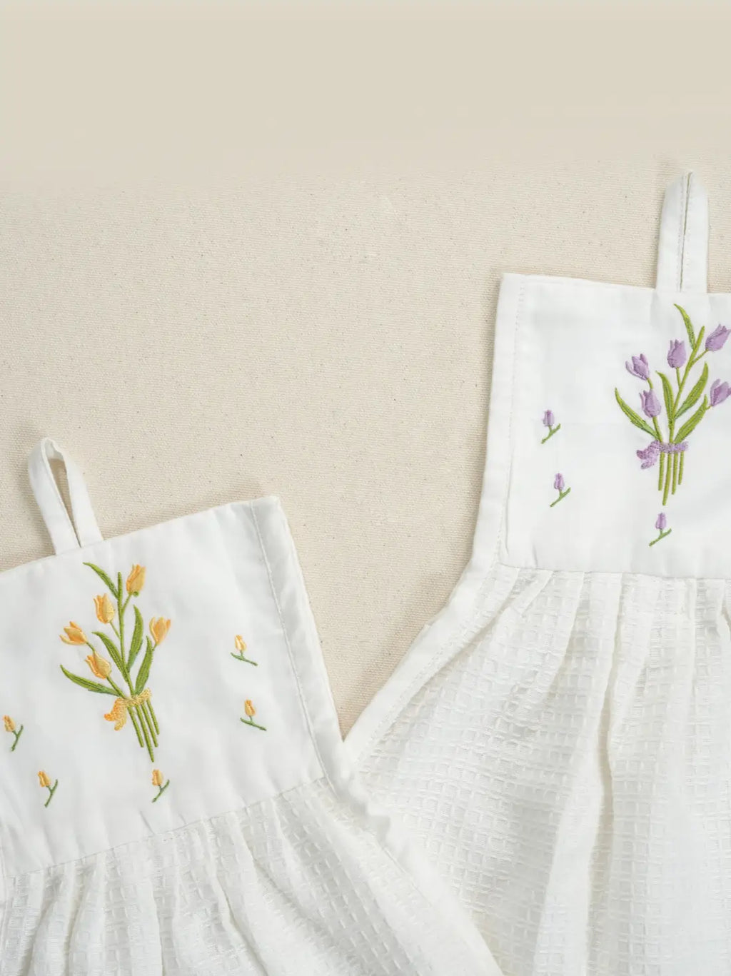 Close-up of yellow and purple tulip bouquets embroidered on two white hanging hand towels