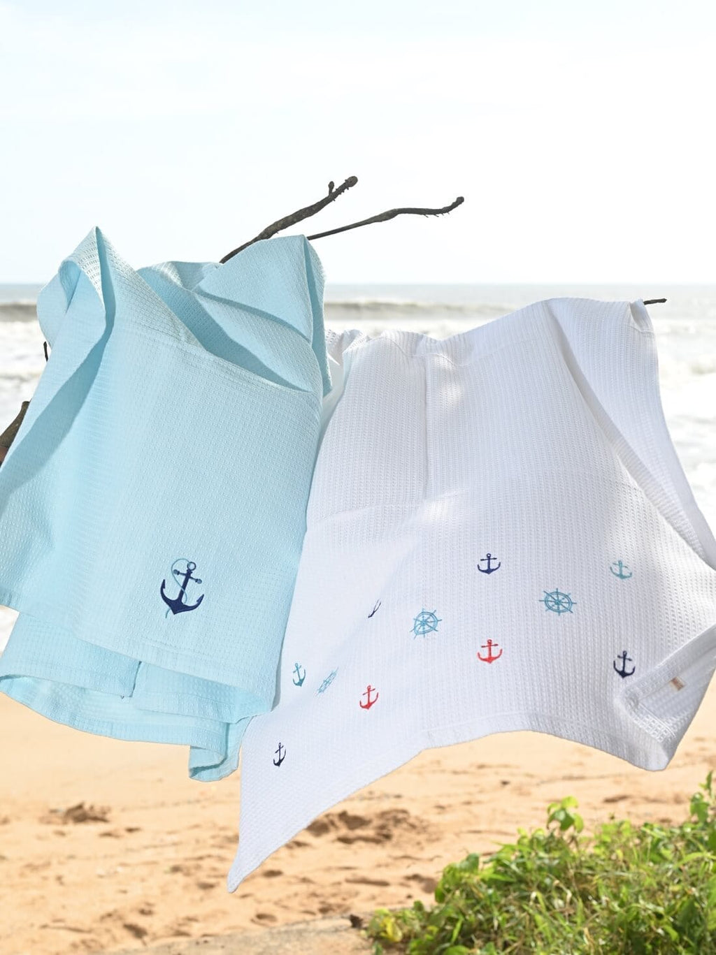 Pale blue and white waffle towels with embroidered anchors and ship wheels hanging by the beach