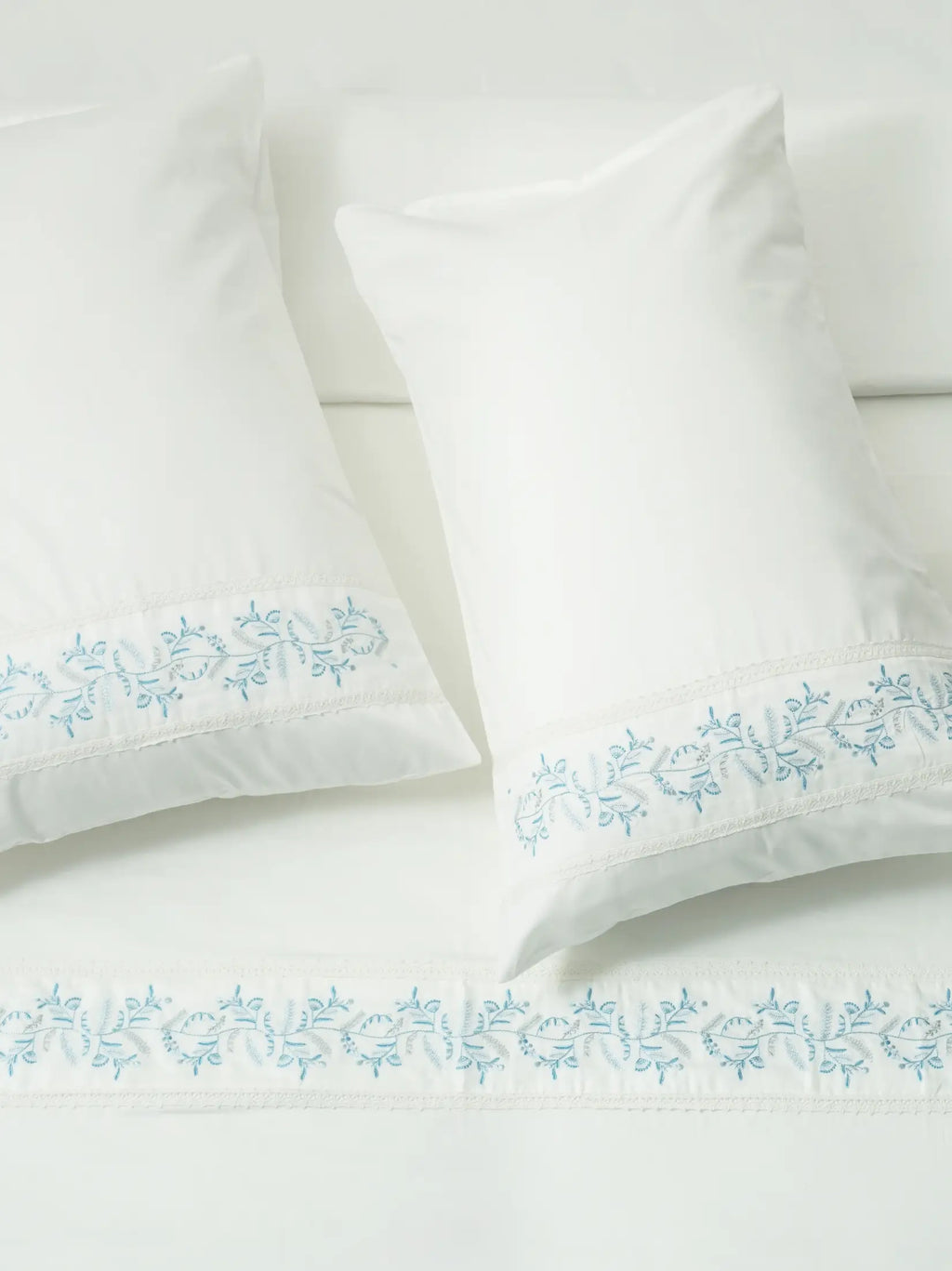 White bed linen and two pillowcases with blue vine embroidery and white lace trim