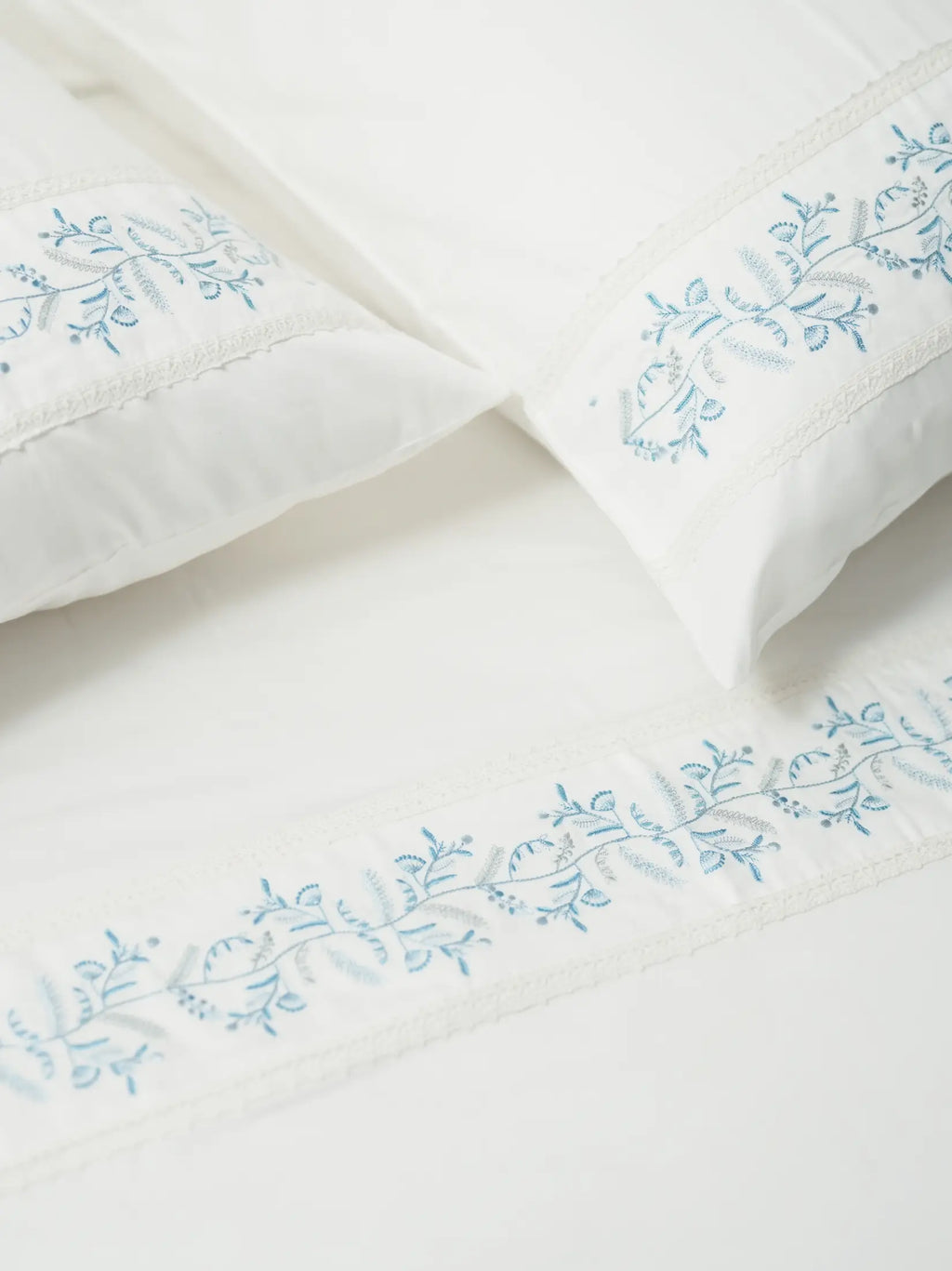 Two white pillowcases and a bed sheet with blue vine embroidery and lace trim