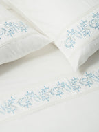 Two white pillowcases and a bed sheet with blue vine embroidery and lace trim