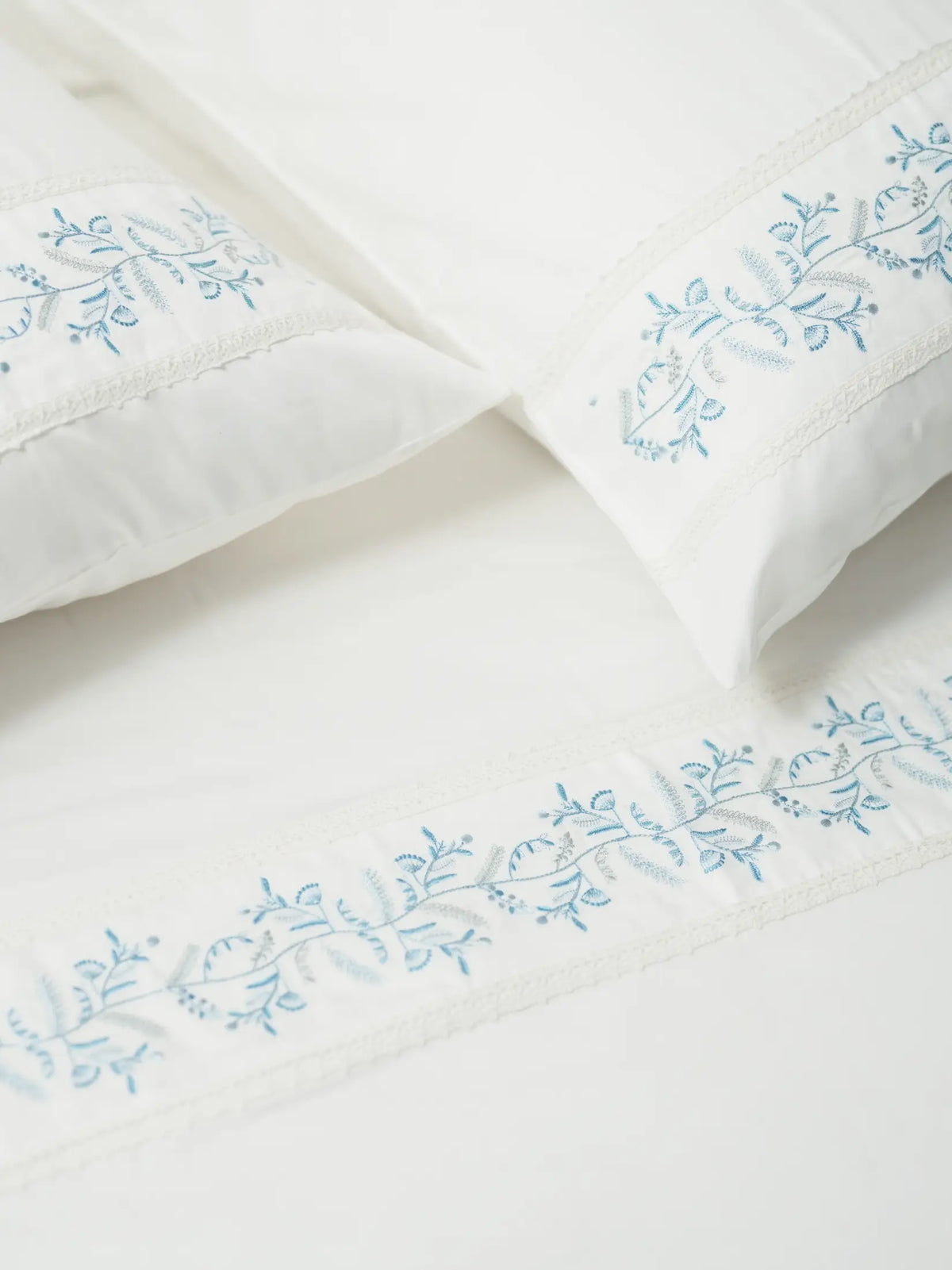 Two white pillowcases and a bed sheet with blue vine embroidery and lace trim