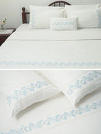 Composite view of white bed linen and pillowcases with blue vine embroidered borders