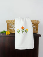 White Kerala bath towel with orange and yellow floral embroidery over a wicker basket