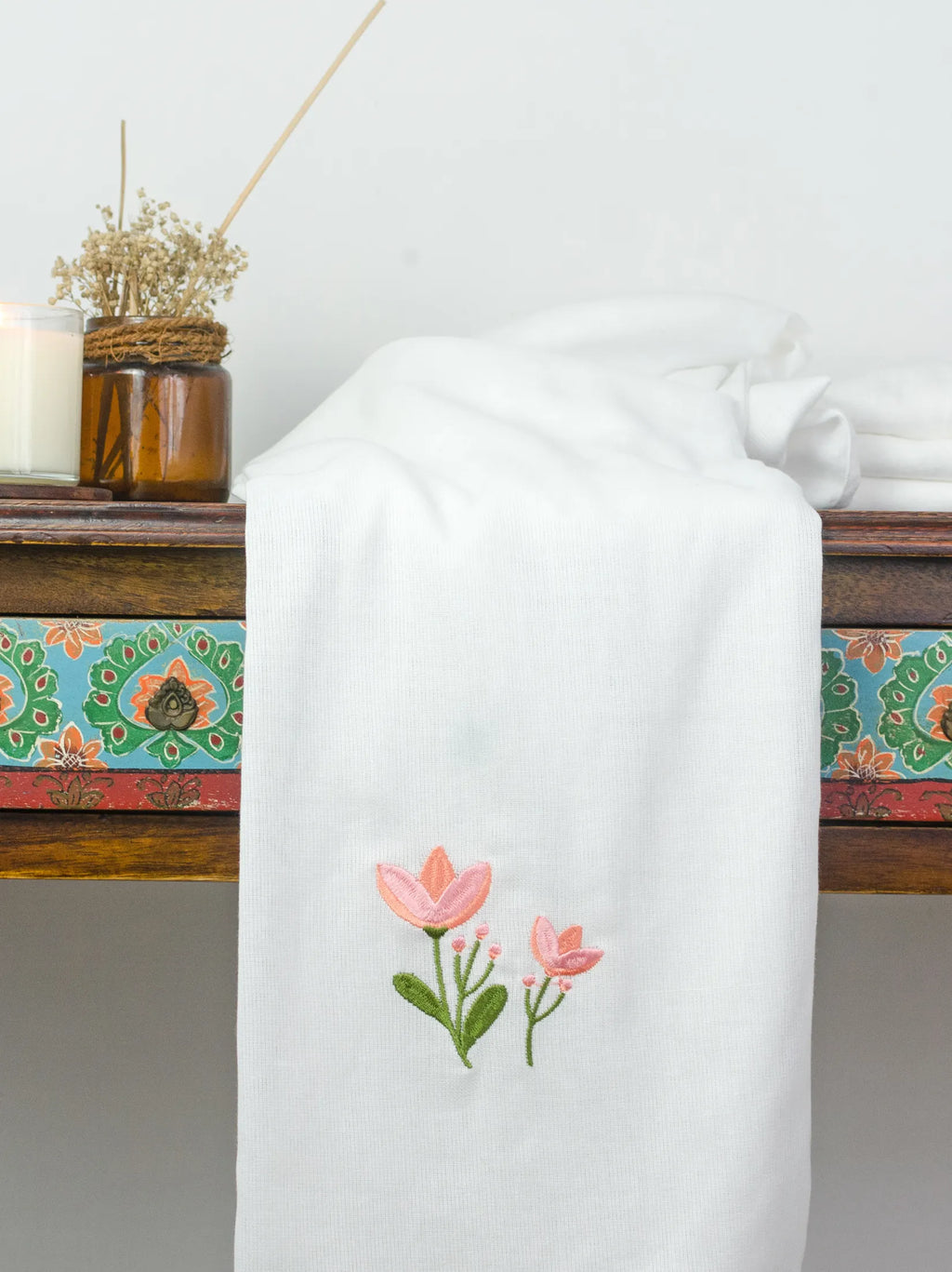 White Kerala bath towel with pink floral embroidery draped over a wooden table