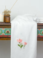 White Kerala bath towel with pink floral embroidery draped over a wooden table