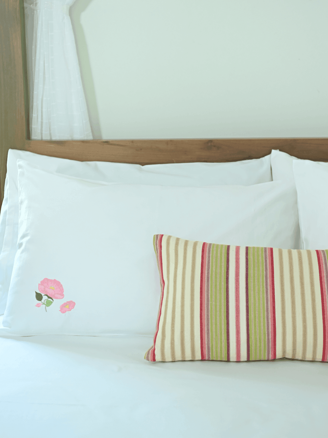 White poppy embroidered pillowcase styled with a striped cushion on a bed